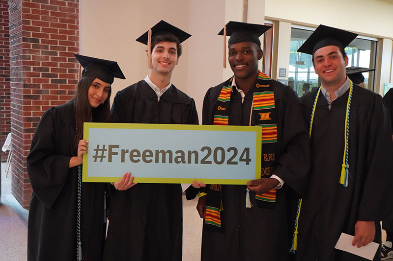 Three freeman undergraduates in cap and gown hold Freeman 2024 sign.