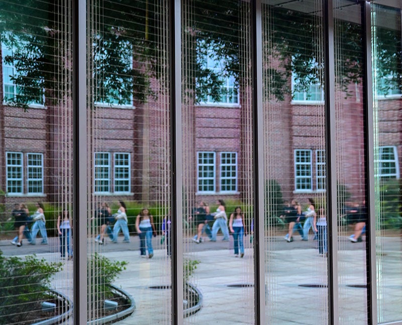 Artistic shot of students reflected in glass of Goldring/Woldenberg Business Complex